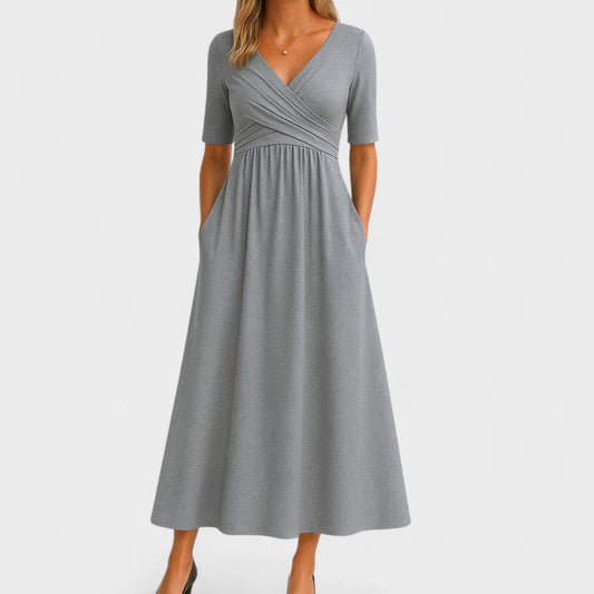 Gray - A woman wearing a heather gray jersey knit midi dress featuring a surplice V-neckline, ruched wrap bodice, short sleeves, and a flowy A-line skirt with side pockets.