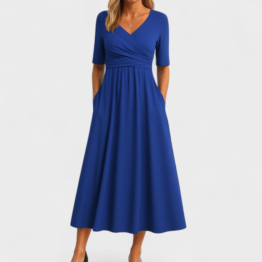 Blue - A woman wearing a heather gray jersey knit midi dress featuring a surplice V-neckline, ruched wrap bodice, short sleeves, and a flowy A-line skirt with side pockets.