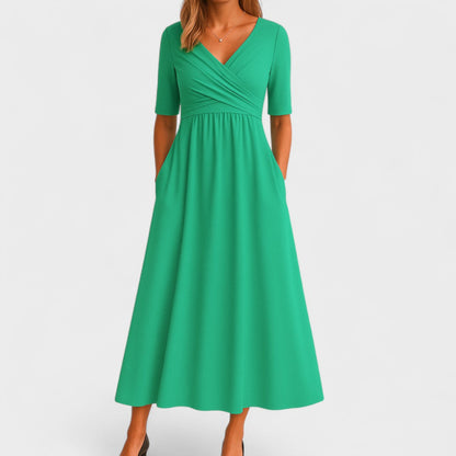 Green - A woman wearing a heather gray jersey knit midi dress featuring a surplice V-neckline, ruched wrap bodice, short sleeves, and a flowy A-line skirt with side pockets.