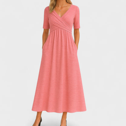 Pink - A woman wearing a heather gray jersey knit midi dress featuring a surplice V-neckline, ruched wrap bodice, short sleeves, and a flowy A-line skirt with side pockets.
