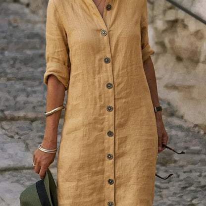 Yellow - A woman wearing a black linen button-down midi dress with roll-up sleeves, a band collar, and ornate gold-tone buttons, walking on a rustic stone street.
