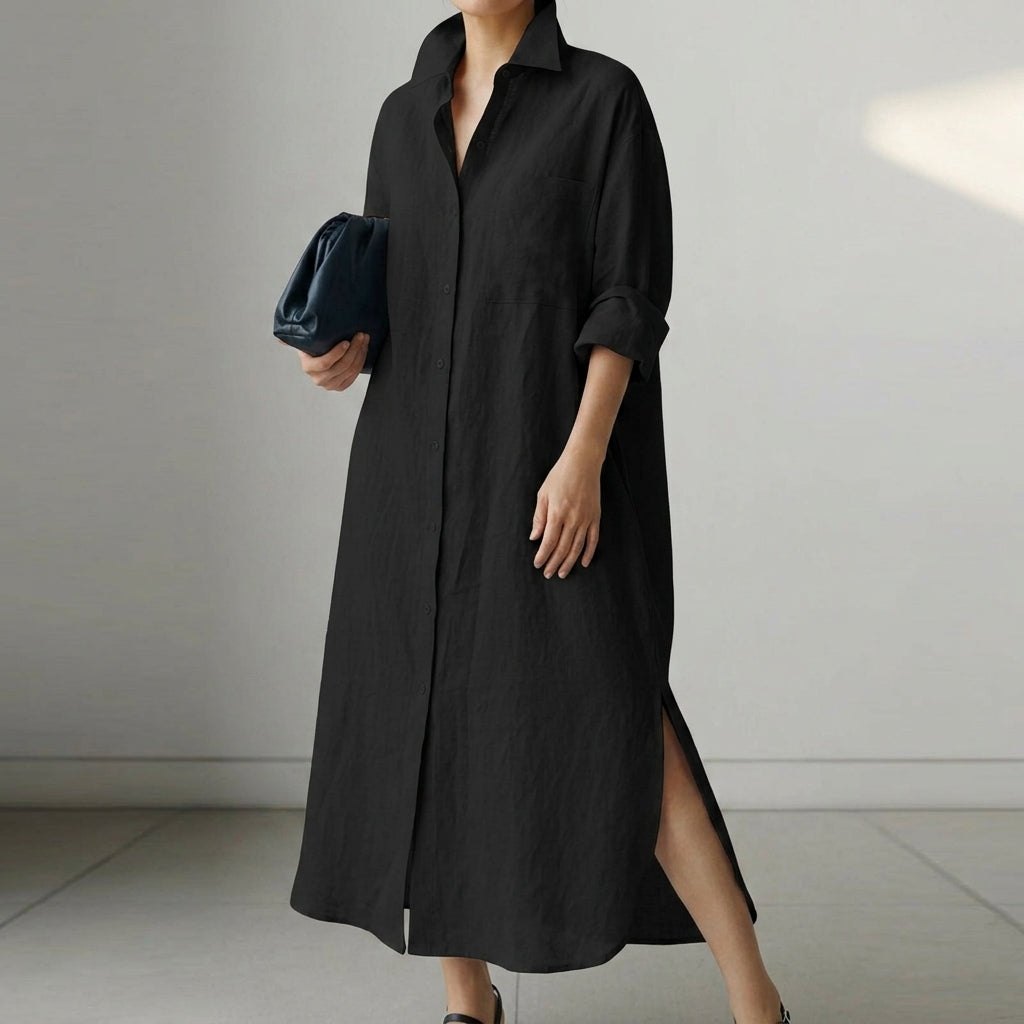 Black - A woman wearing a black, relaxed-fit linen maxi shirt dress with a collared neckline, button-down front, rolled-up sleeves, and high side slits, paired with a dark blue clutch bag.