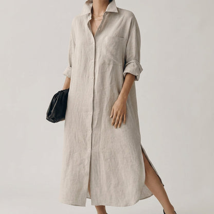 Beige - A woman wearing a black, relaxed-fit linen maxi shirt dress with a collared neckline, button-down front, rolled-up sleeves, and high side slits, paired with a dark blue clutch bag.