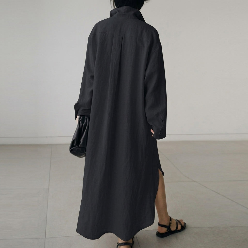 Beige - A woman wearing a black, relaxed-fit linen maxi shirt dress with a collared neckline, button-down front, rolled-up sleeves, and high side slits, paired with a dark blue clutch bag.