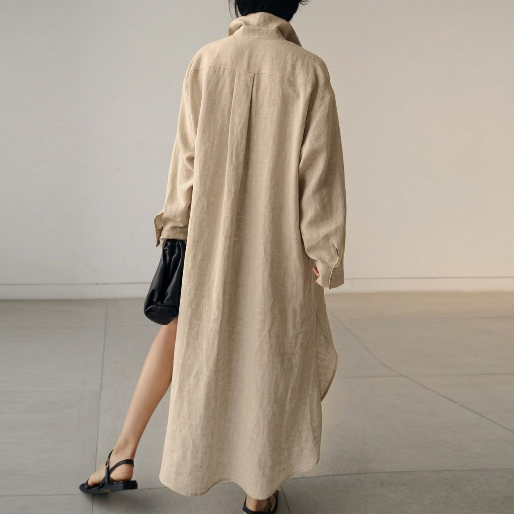 Beige - A woman wearing a black, relaxed-fit linen maxi shirt dress with a collared neckline, button-down front, rolled-up sleeves, and high side slits, paired with a dark blue clutch bag.