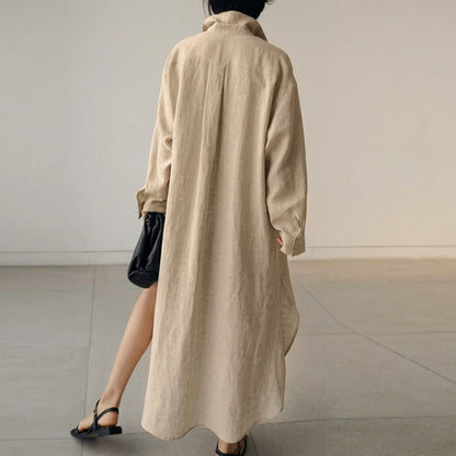 Beige - A woman wearing a black, relaxed-fit linen maxi shirt dress with a collared neckline, button-down front, rolled-up sleeves, and high side slits, paired with a dark blue clutch bag.