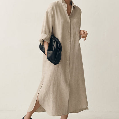 Beige - A woman wearing a black, relaxed-fit linen maxi shirt dress with a collared neckline, button-down front, rolled-up sleeves, and high side slits, paired with a dark blue clutch bag.