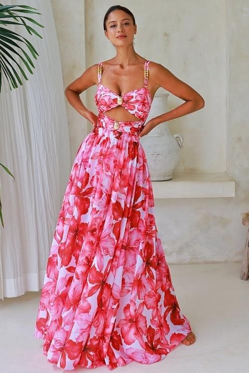 Woman in pink and red floral chiffon maxi dress with cutout waist.
