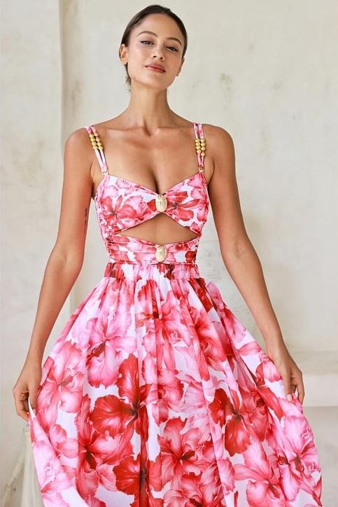 Woman in pink and red floral chiffon maxi dress with cutout waist.