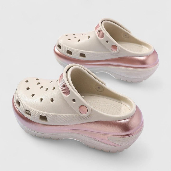 Molded foam slip-on platform clogs featuring ventilation ports across the upper, a pivoting heel strap, and a distinct metallic trim along the thick midsole