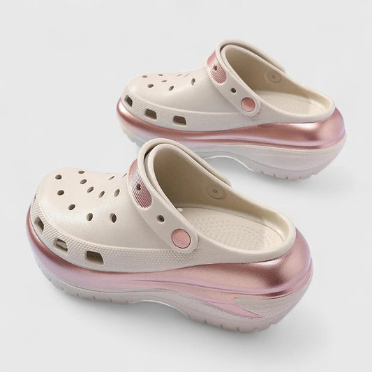 Molded foam slip-on platform clogs featuring ventilation ports across the upper, a pivoting heel strap, and a distinct metallic trim along the thick midsole