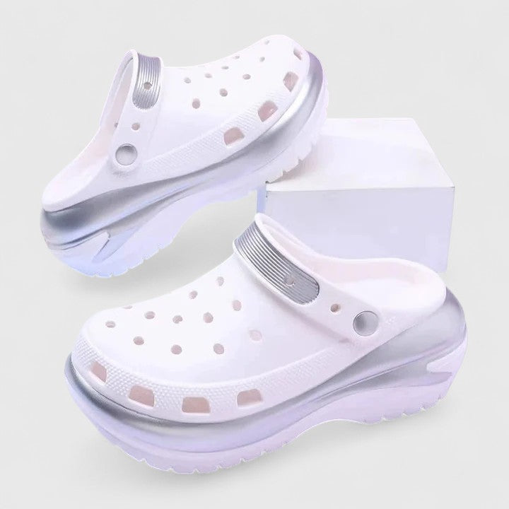 White - Molded foam slip-on platform clogs featuring ventilation ports across the upper, a pivoting heel strap, and a distinct metallic trim along the thick midsole