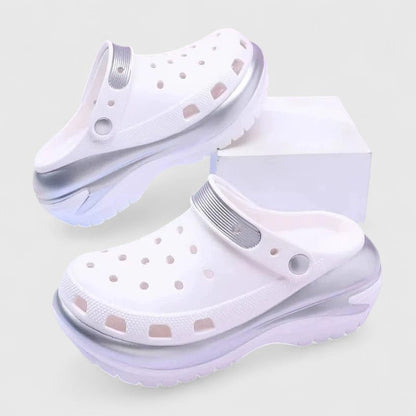 White - Molded foam slip-on platform clogs featuring ventilation ports across the upper, a pivoting heel strap, and a distinct metallic trim along the thick midsole