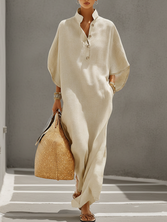 Oatmeal - Woman walking outdoors wearing a long oversized woven maxi dress featuring a structured collar, half-button front, wide sleeves, and side pockets.