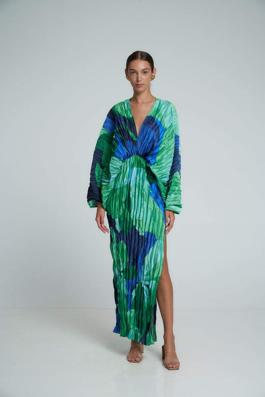 Woman wearing a long green and blue pleated dress with a V-neck and a slit.
