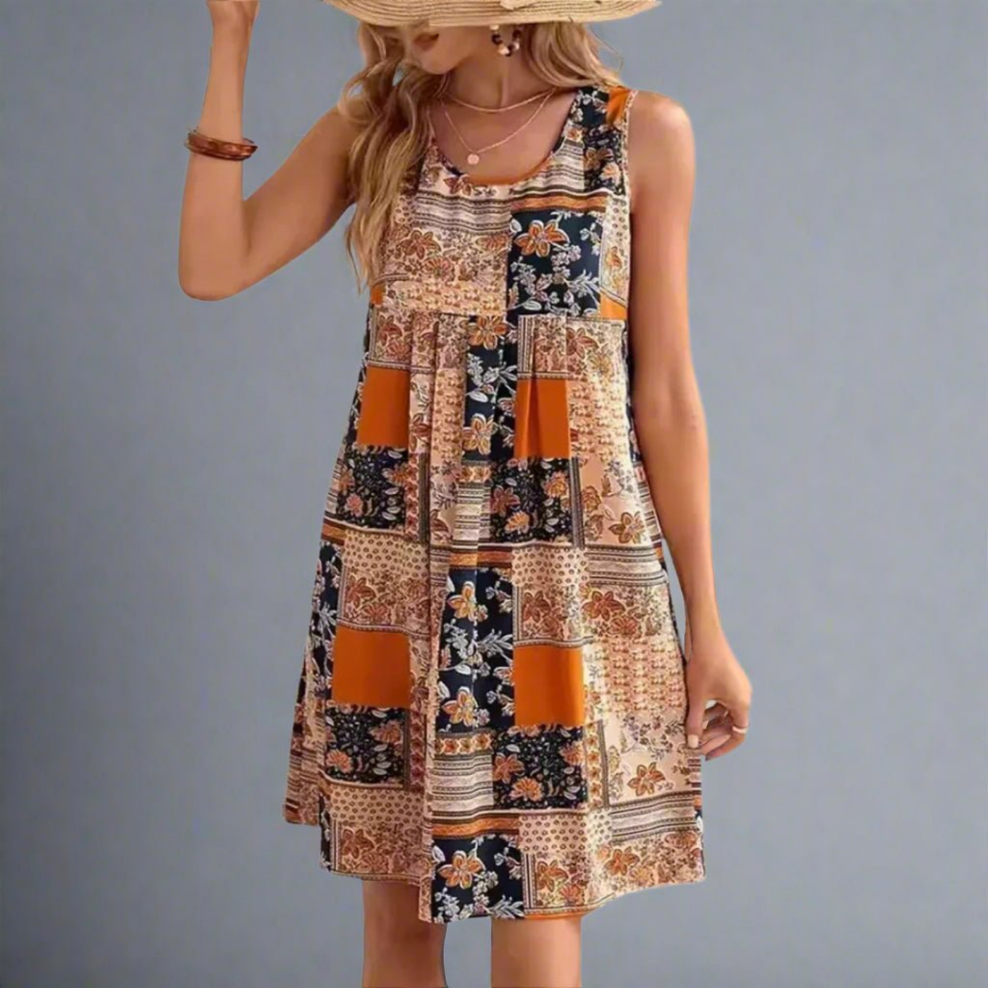 Orange - A woman wearing a sleeveless mini dress featuring a multi-colored patchwork floral print in orange, navy, and cream, styled with a scoop neckline and a gathered empire waist.