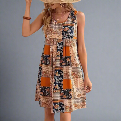 Orange - A woman wearing a sleeveless mini dress featuring a multi-colored patchwork floral print in orange, navy, and cream, styled with a scoop neckline and a gathered empire waist.