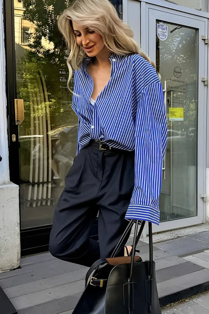 Woman wearing oversized blue and white striped shirt with black pants and sunglasses