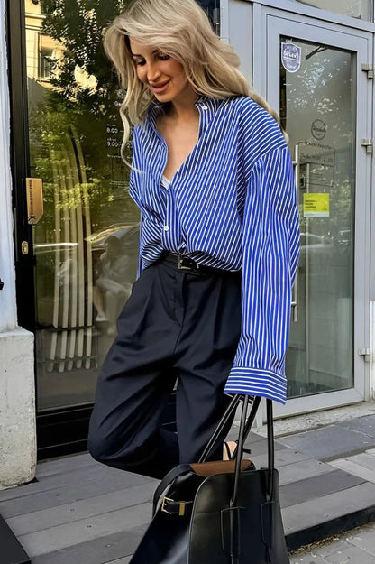 Woman wearing oversized blue and white striped shirt with black pants and sunglasses