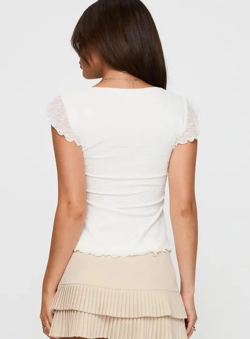 Woman wearing white textured cotton top with ruffle sleeves and tie front