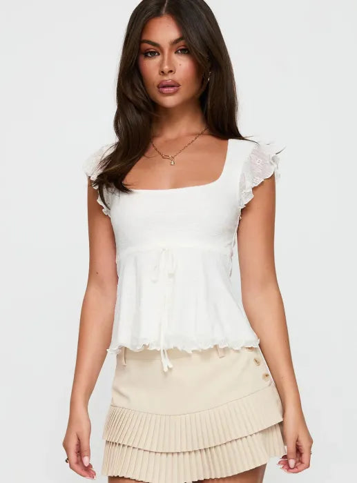 Woman wearing white textured cotton top with ruffle sleeves and tie front