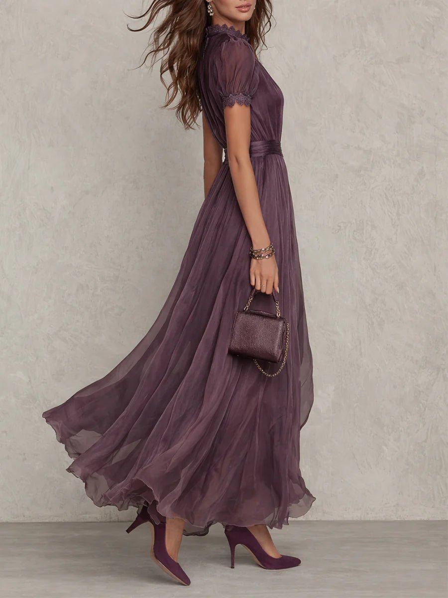Purple - A woman wearing a flowing, deep mauve pleated chiffon maxi dress with a high keyhole neckline, lace-trimmed puff sleeves, and a banded waist.