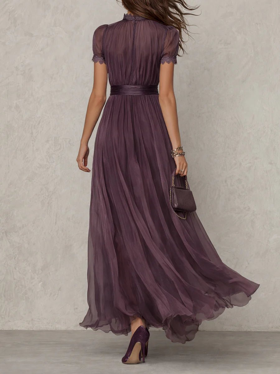 Purple - A woman wearing a flowing, deep mauve pleated chiffon maxi dress with a high keyhole neckline, lace-trimmed puff sleeves, and a banded waist.