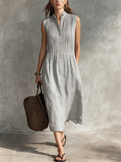 Grey - Woman wearing a sleeveless midi shirtdress with a pleated button-front bodice and stand collar, carrying a woven tote bag.