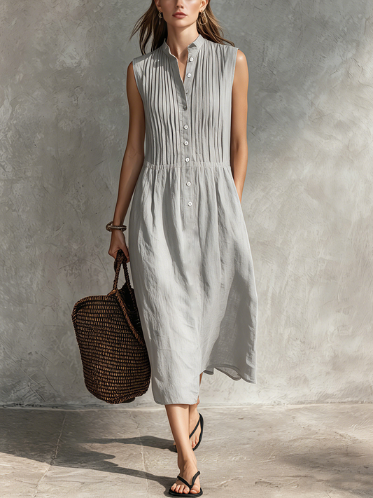Grey - Woman wearing a sleeveless midi shirtdress with a pleated button-front bodice and stand collar, carrying a woven tote bag.