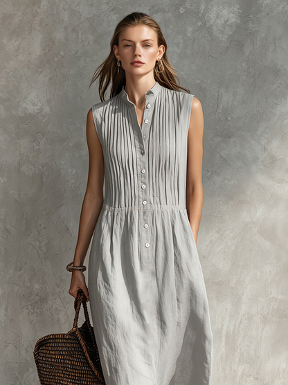 Grey - Woman wearing a sleeveless midi shirtdress with a pleated button-front bodice and stand collar, carrying a woven tote bag.