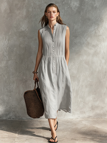 Grey - Woman wearing a sleeveless midi shirtdress with a pleated button-front bodice and stand collar, carrying a woven tote bag.
