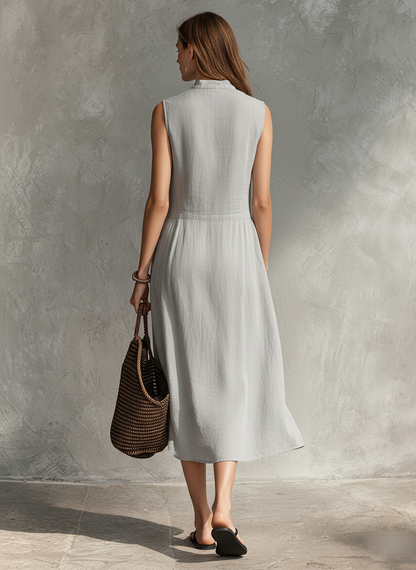 Grey - Woman wearing a sleeveless midi shirtdress with a pleated button-front bodice and stand collar, carrying a woven tote bag.