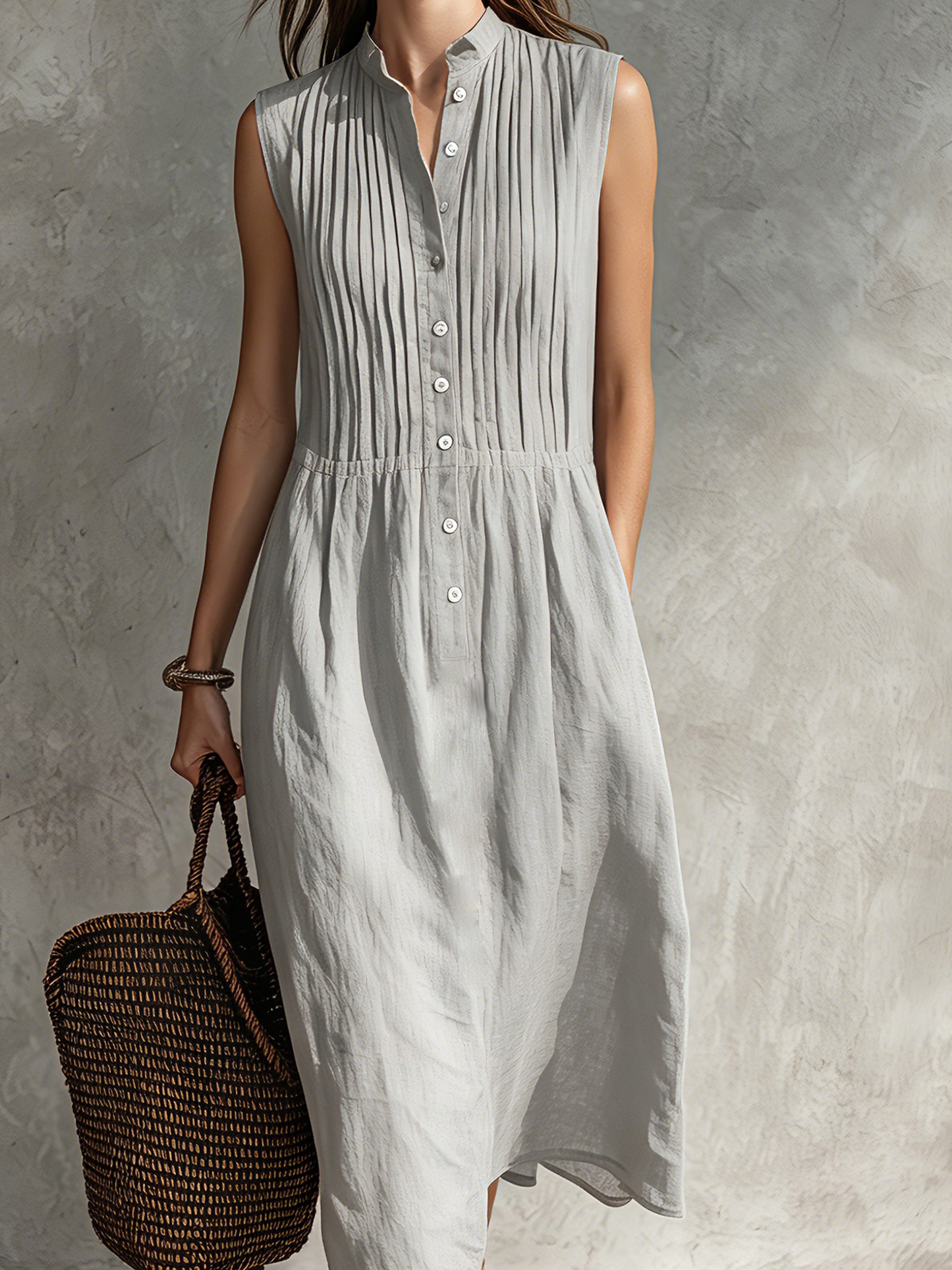 Grey - Woman wearing a sleeveless midi shirtdress with a pleated button-front bodice and stand collar, carrying a woven tote bag.