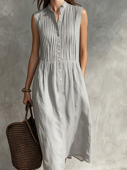 Grey - Woman wearing a sleeveless midi shirtdress with a pleated button-front bodice and stand collar, carrying a woven tote bag.