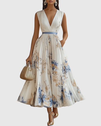 White - Model wearing a sleeveless, plunging V-neck midi dress in pleated off-white chiffon with a blue and gold watercolor floral print, featuring a cinched blue waist band and a flowy A-line skirt with pockets.