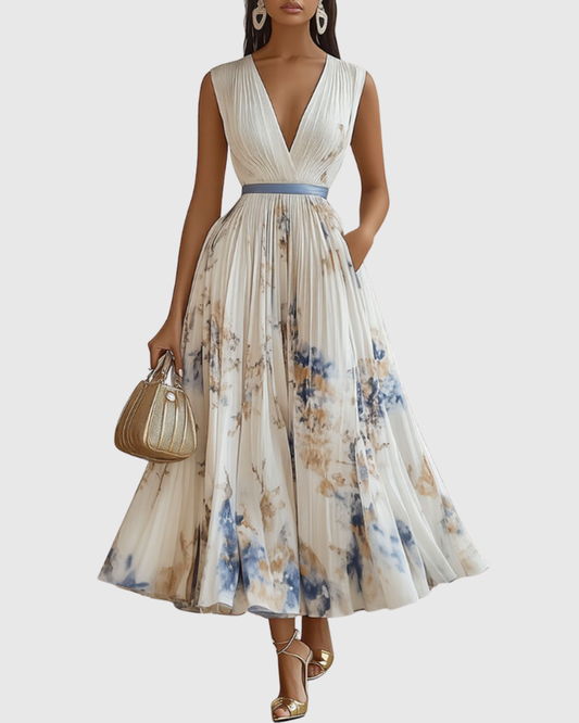 White - Model wearing a sleeveless, plunging V-neck midi dress in pleated off-white chiffon with a blue and gold watercolor floral print, featuring a cinched blue waist band and a flowy A-line skirt with pockets.