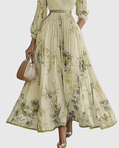 Yellow - Model wearing a sleeveless, plunging V-neck midi dress in pleated off-white chiffon with a blue and gold watercolor floral print, featuring a cinched blue waist band and a flowy A-line skirt with pockets.