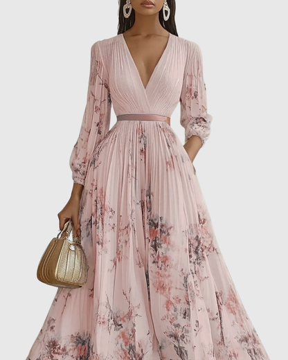 Pink - Model wearing a sleeveless, plunging V-neck midi dress in pleated off-white chiffon with a blue and gold watercolor floral print, featuring a cinched blue waist band and a flowy A-line skirt with pockets.