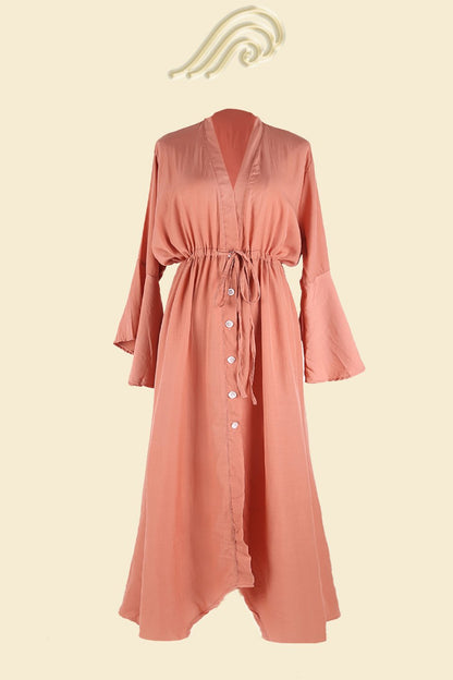 Woman in terracotta gauze maxi dress with tie waist and bell sleeves.