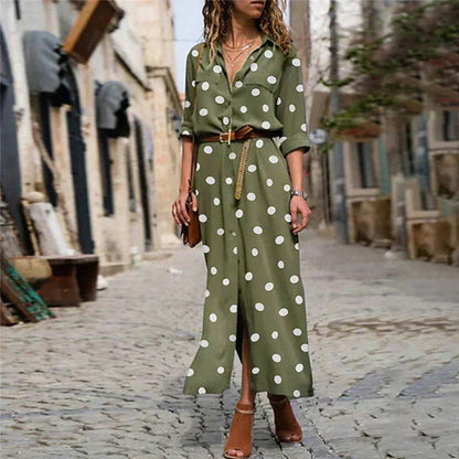Army Green - Woman wearing an olive green maxi shirt dress with white polka dots, featuring a collared button-down front, rolled-up long sleeves, and a brown belt, walking on a cobblestone street.