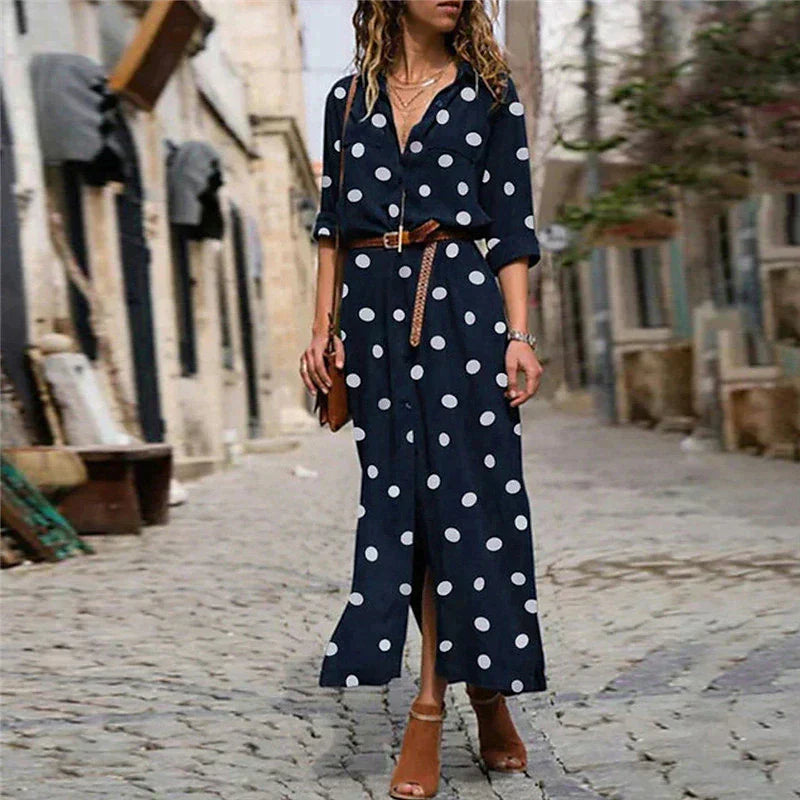 Navy Blue - Woman wearing an olive green maxi shirt dress with white polka dots, featuring a collared button-down front, rolled-up long sleeves, and a brown belt, walking on a cobblestone street.