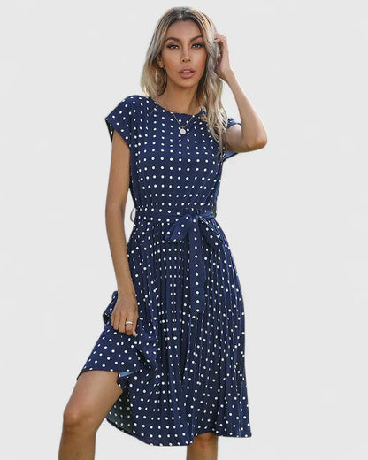 Blue - A woman wearing a dusty pink midi dress with white polka dots, featuring cap sleeves, a belted waist, and a pleated skirt.