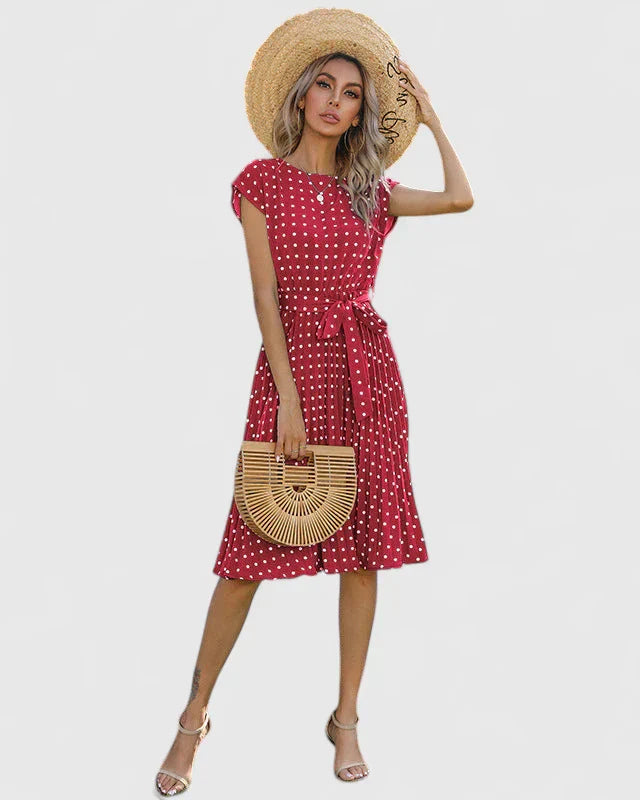 Red - A woman wearing a dusty pink midi dress with white polka dots, featuring cap sleeves, a belted waist, and a pleated skirt.