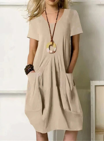 Beige - Woman wearing a solid color short sleeve knee-length shift dress featuring front pleats and two large patch pockets