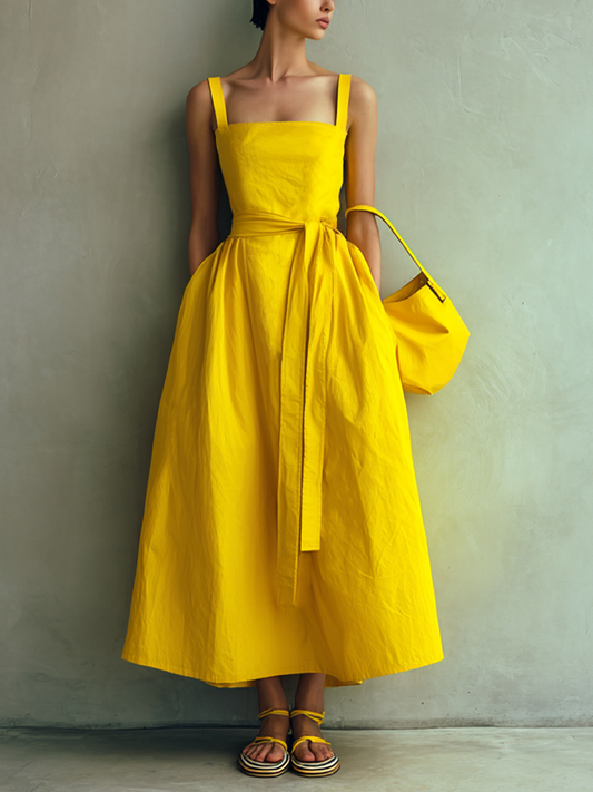 Yellow - Woman wearing a square-neck midi dress with wide straps, a self-tie waist, and a voluminous A-line skirt, holding a matching handbag against a textured grey background.