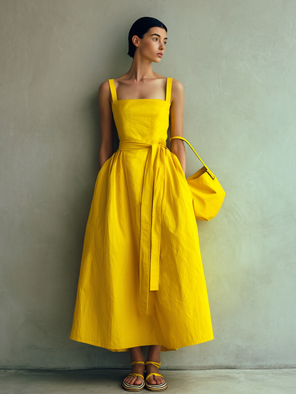 Yellow - Woman wearing a square-neck midi dress with wide straps, a self-tie waist, and a voluminous A-line skirt, holding a matching handbag against a textured grey background.