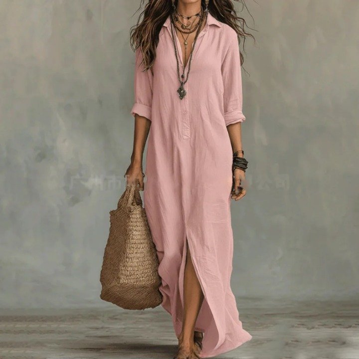 Pink - A woman wearing a relaxed-fit white linen maxi sundress with a pointed collar, button placket, and front slit, carrying a woven straw bag.