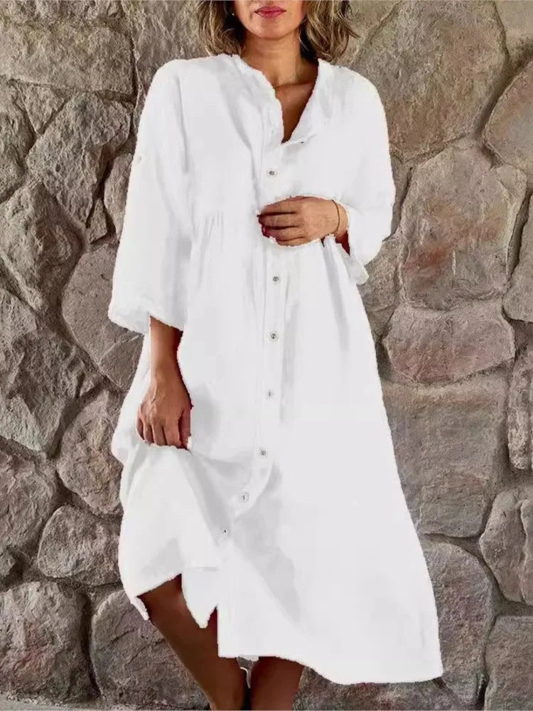 White - A woman wearing a vibrant fuchsia pink linen midi dress with a button-down front, roll-tab sleeves, and an empire waist, standing against a stone wall.