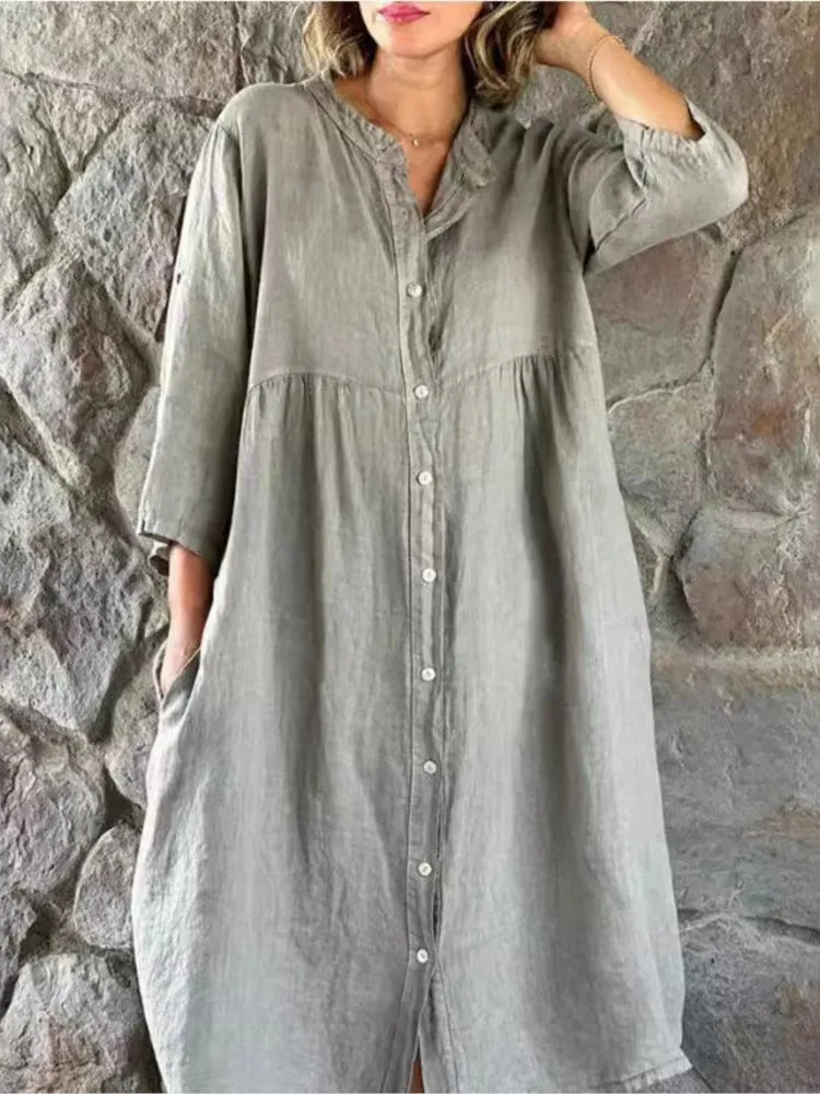 Gray - A woman wearing a vibrant fuchsia pink linen midi dress with a button-down front, roll-tab sleeves, and an empire waist, standing against a stone wall.