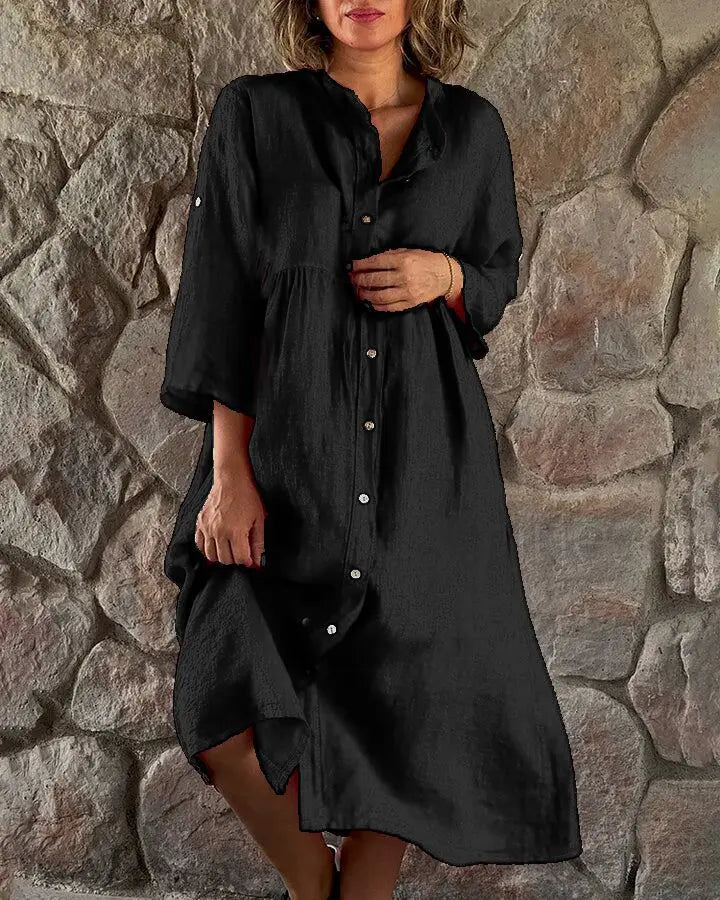 Black - A woman wearing a vibrant fuchsia pink linen midi dress with a button-down front, roll-tab sleeves, and an empire waist, standing against a stone wall.